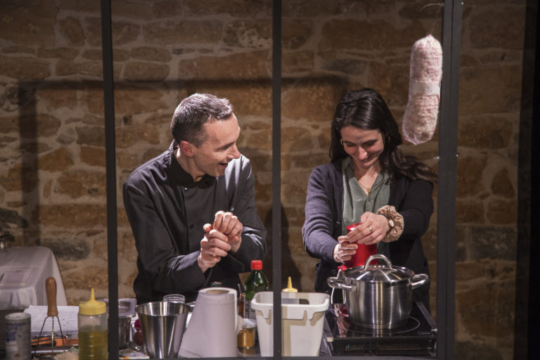 Deux interprètes préparent un repas dans une cuisine aux murs de pierre. Entre les gestes simples, les sourires échangés et la vapeur qui s'élève de la casserole, la scène fait naître une atmosphère chaleureuse où l'intime se révèle peu à peu.