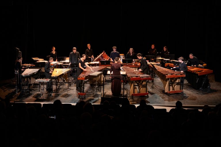 Une quinzaine d’interprètes occupent la scène entourés de marimbas, vibraphones, timbales et autres instruments de percussion. L’organisation de l’ensemble, centrée autour de la direction d’orchestre, met en valeur l’ampleur de cette formation singulière